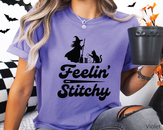 Feelin’ Stitchy Halloween t-shirt design featuring a black Stitch Witch silhouette, black cat, broom, and spool of thread in a playful sewing-themed design.