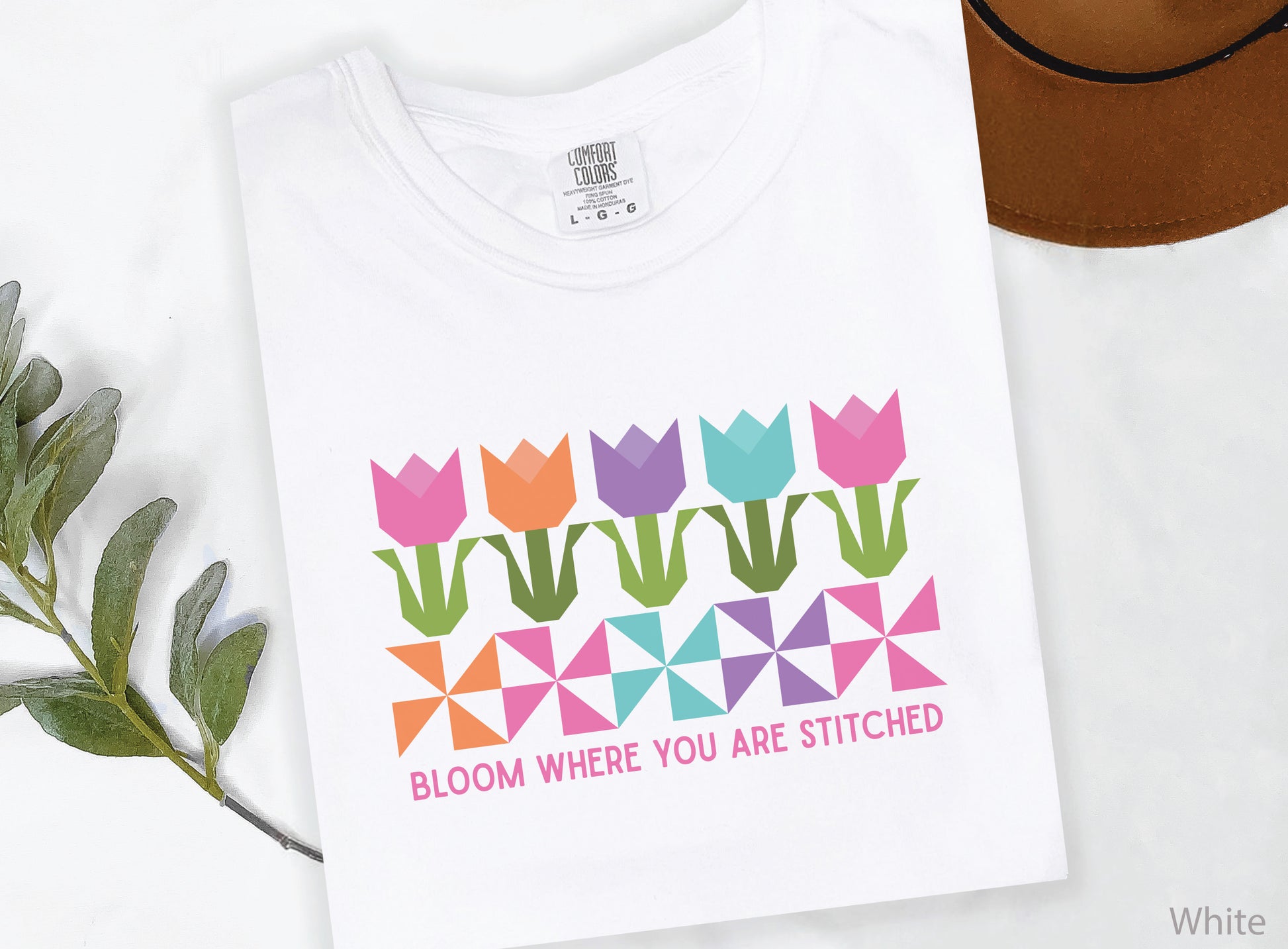 Quilting t-shirt with colorful tulip quilt blocks and pinwheel designs featuring the phrase “Bloom Where You Are Stitched,” perfect for quilters and sewing lovers.