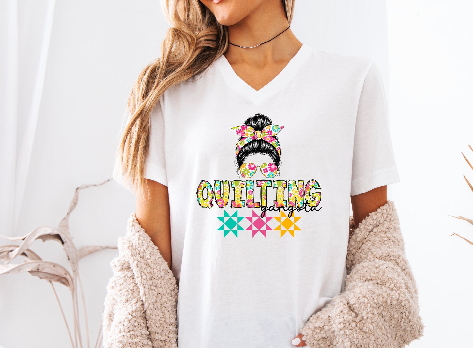 White t-shirt featuring a stylish messy bun with a floral headband and sunglasses above the words "Quilting Gangsta," accented with colorful quilt blocks, perfect for quilters with a playful sense of humor.