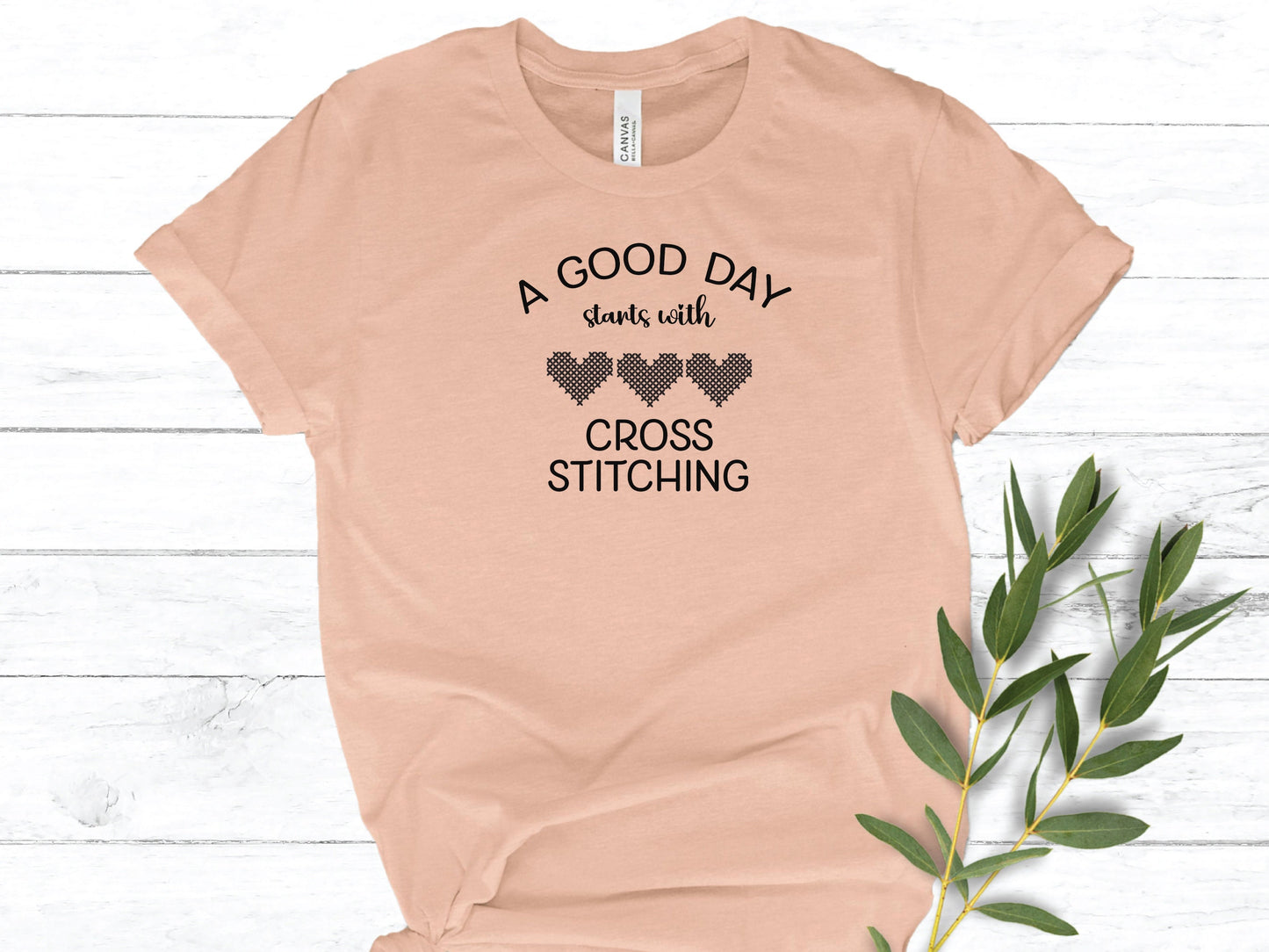 A Good Day Starts With Cross Stitching shirt, with 3 hearts printed on a peach shirt.