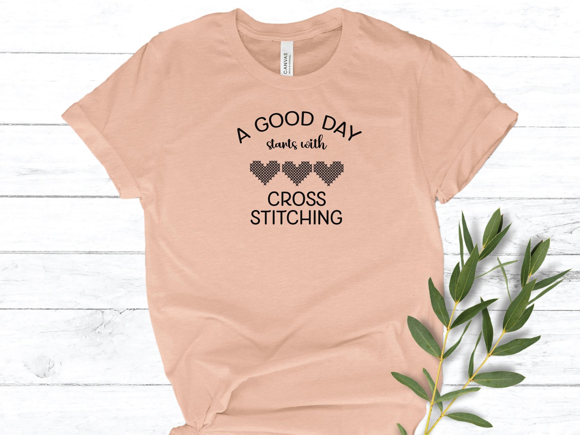 A Good Day Starts With Cross Stitching shirt, with 3 hearts printed on a peach shirt.
